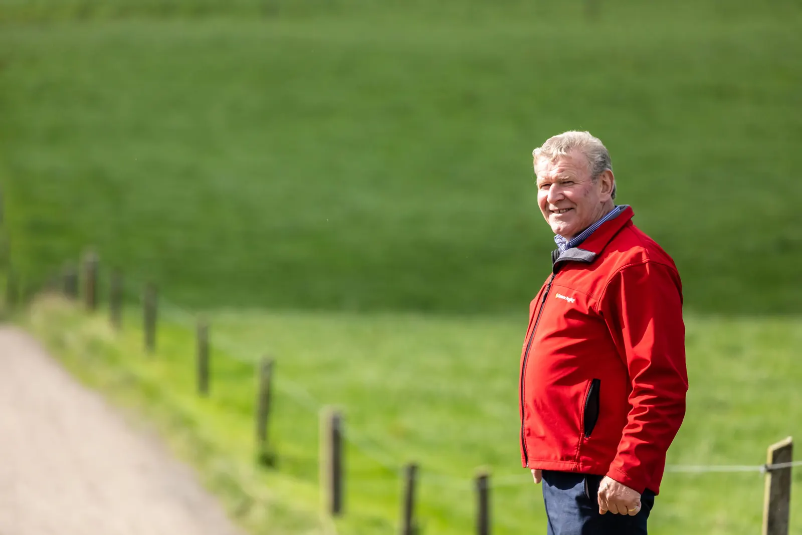Man in a red jacket standing beside a farm lane in a green field